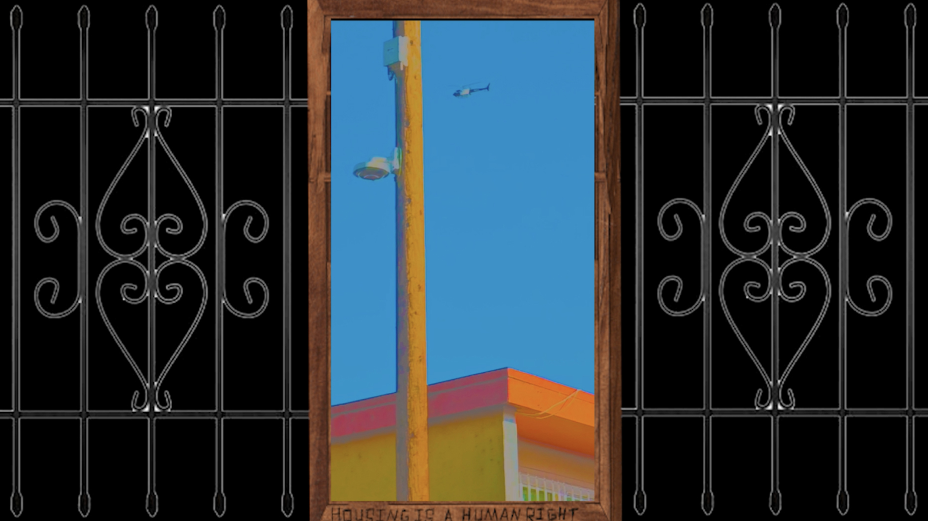 Video Still of a gate over a black background with a building structure and telephone pole with a blue sky containing a small helicopter
