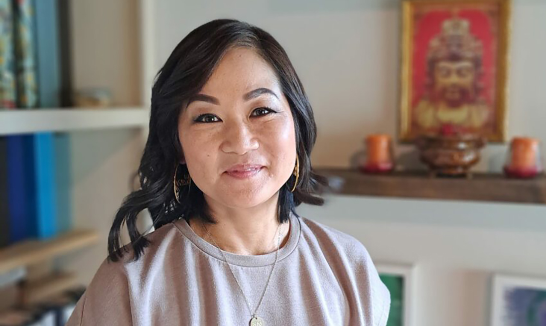 Woman with dark shoulder length hair smiling facing the camera with an image of a Buddhist head in the background